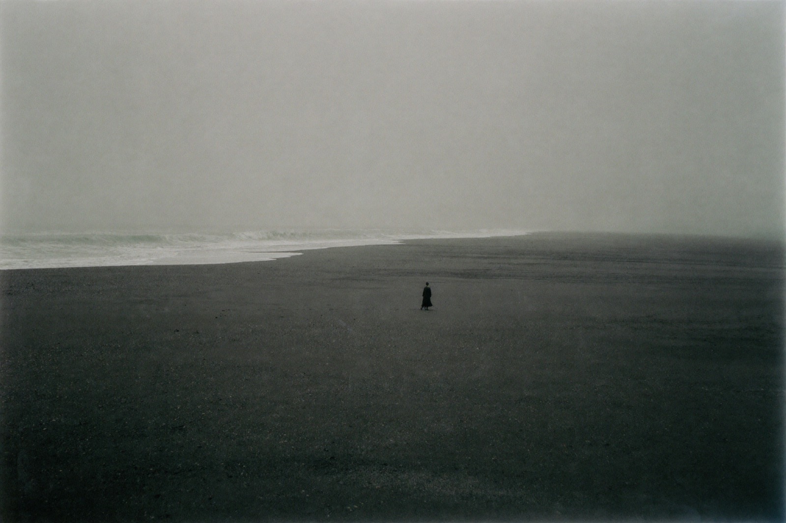 Lone figure in a dark coat on a black sand beach