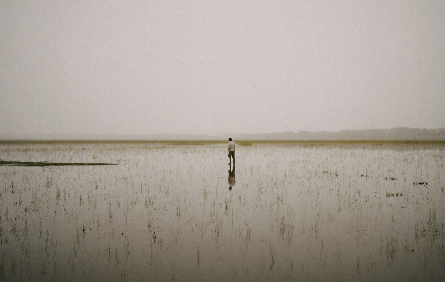 Figure standing in a flooded field mirroring the sky